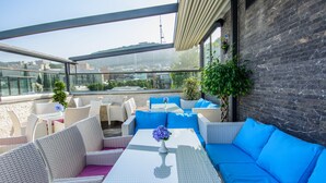 Une terrasse sur le toit, aménagée avec des meubles en osier, une table en verre et offrant une vue sur le paysage urbain.
