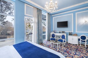 A hotel room with a large bed, a desk with two chairs, a television, and a chandelier. - River Side Hotel (Tbilisi)