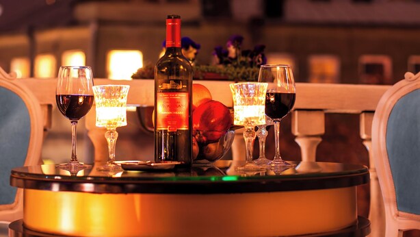 A table with a bottle and glasses of red wine, set against a view of the Eiffel Tower at night. - River Side Hotel (Tbilisi)