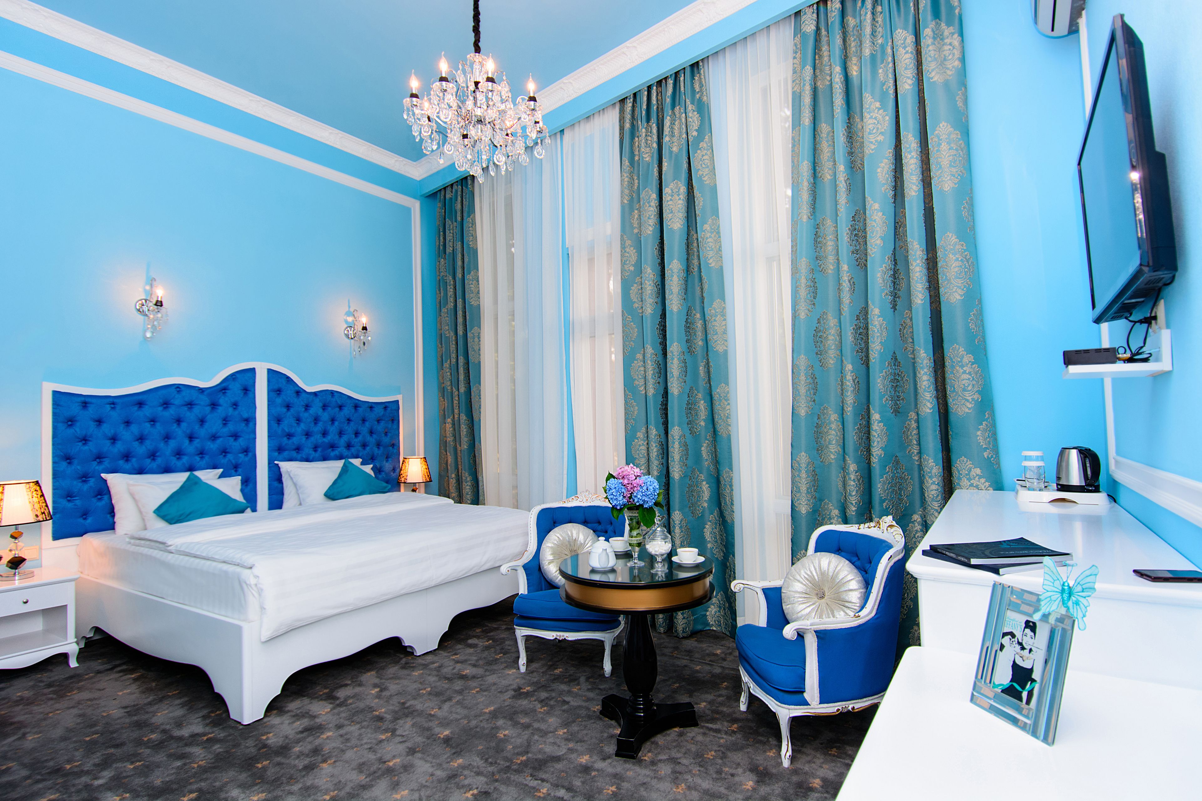 Een hotelkamer met een groot bed, twee stoelen, een tafeltje, een televisie en een kroonluchter.