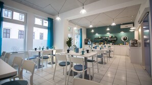 Un café moderne avec des tables et des chaises blanches, des rideaux turquoise et des luminaires suspendus.