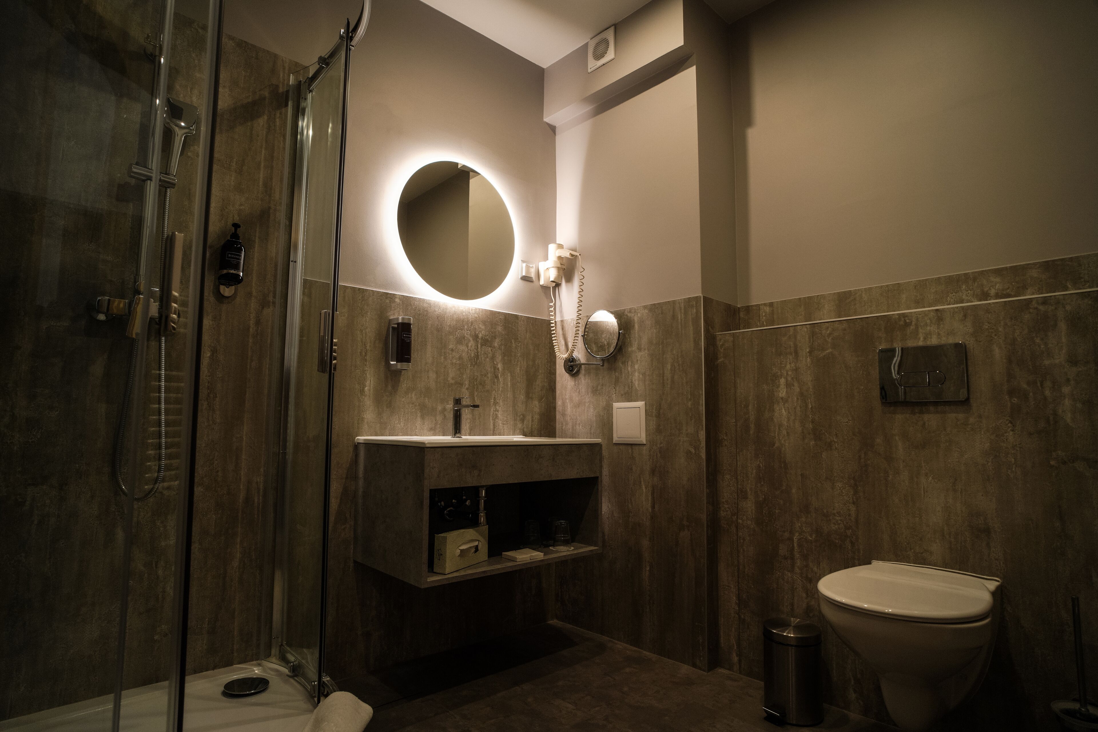 A modern bathroom with a glass-enclosed shower, a round mirror, a toilet, and a vanity with a sink.