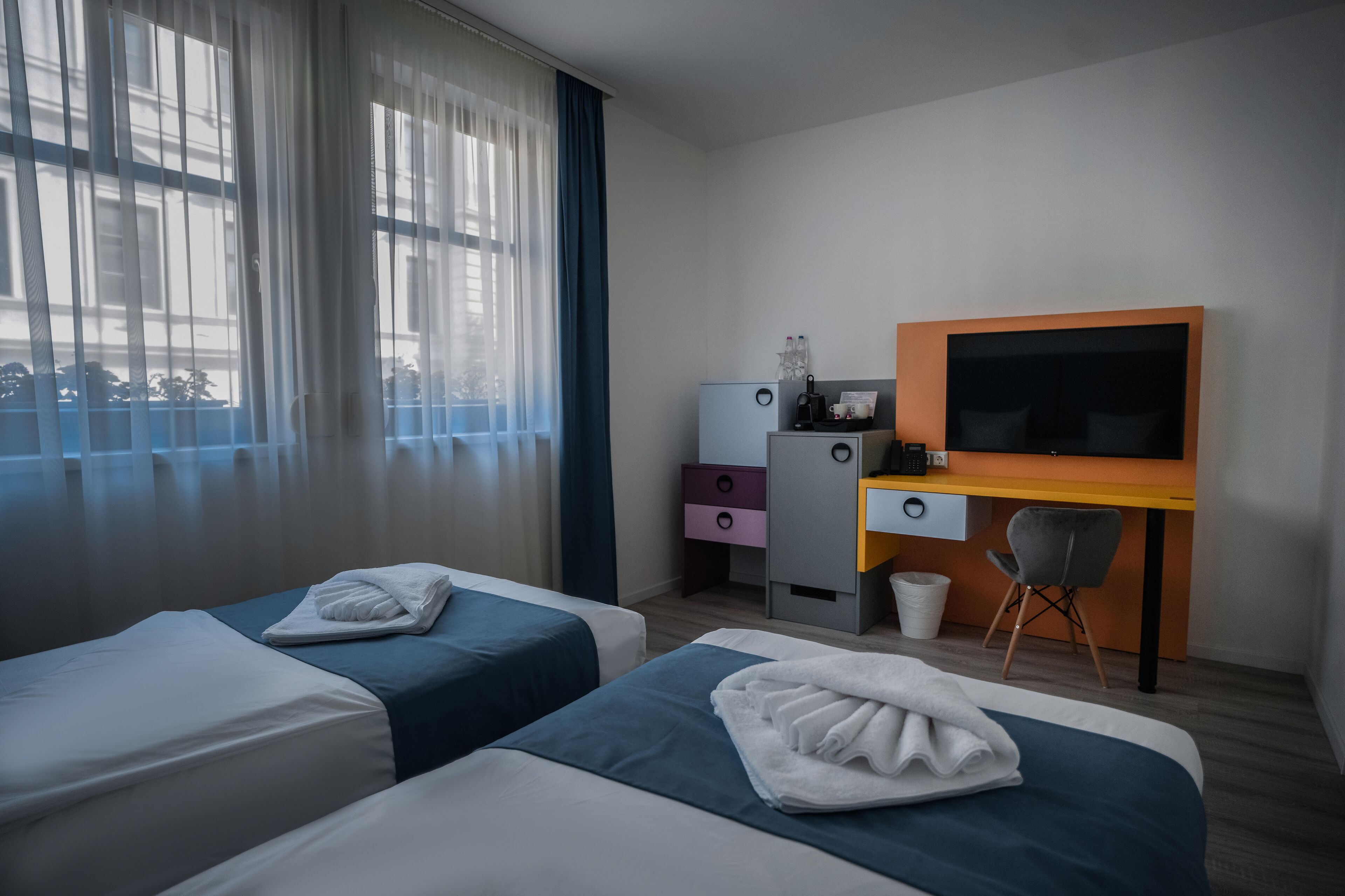 Habitación de hotel con dos camas, un escritorio, una televisión y una ventana con cortinas.