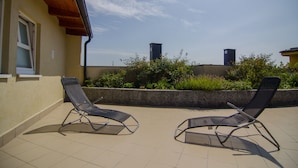 Un espace extérieur aménagé avec deux fauteuils confortables et une vue sur les bâtiments et la verdure en arrière-plan.