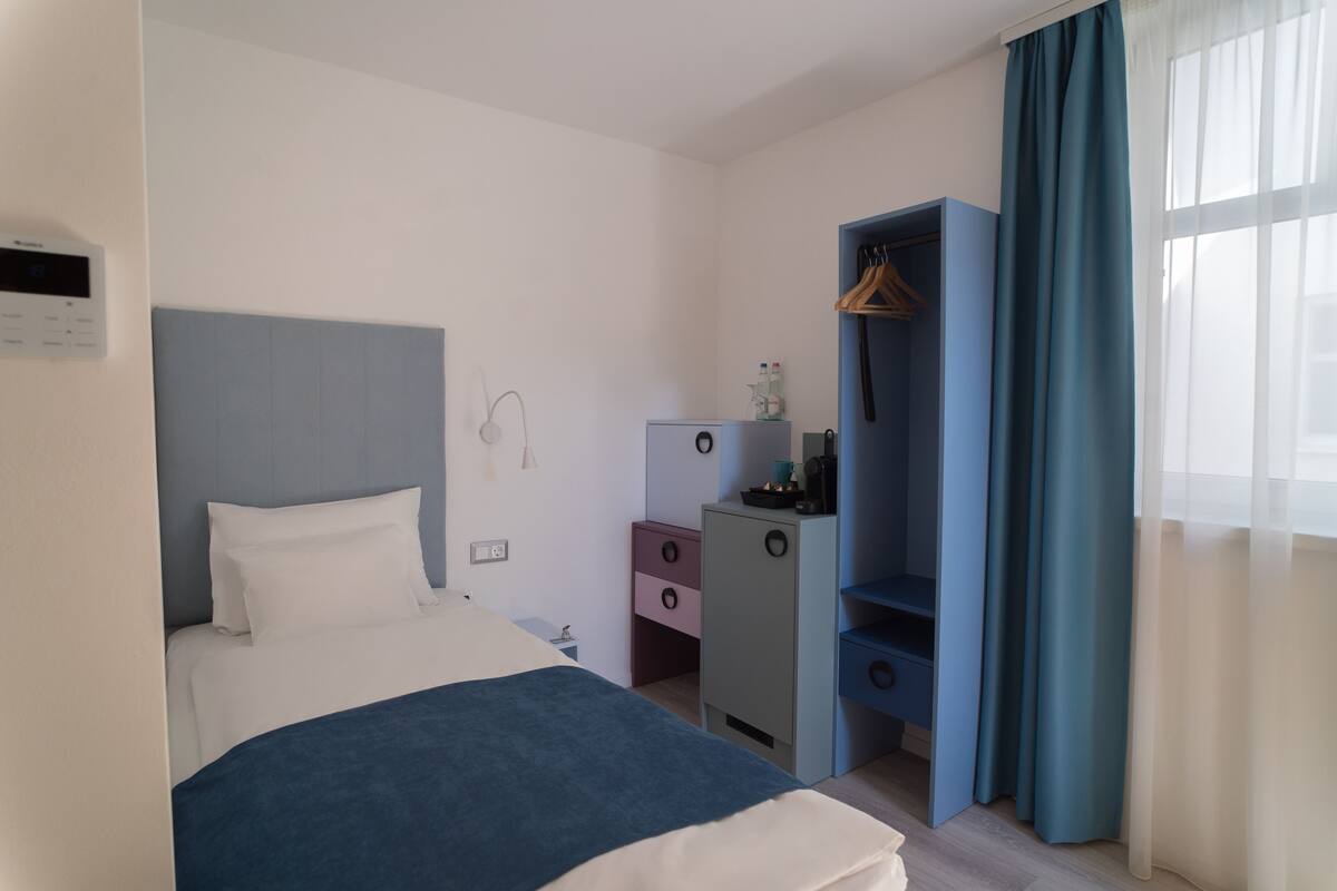 Une chambre d’hôtel avec un lit, un bureau, une armoire et une fenêtre avec des rideaux.
