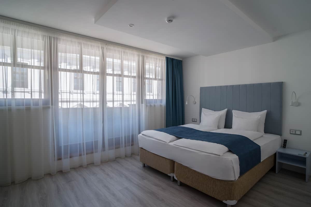 Une chambre moderne avec un grand lit, une table de chevet et une fenêtre ornée de rideaux légers.