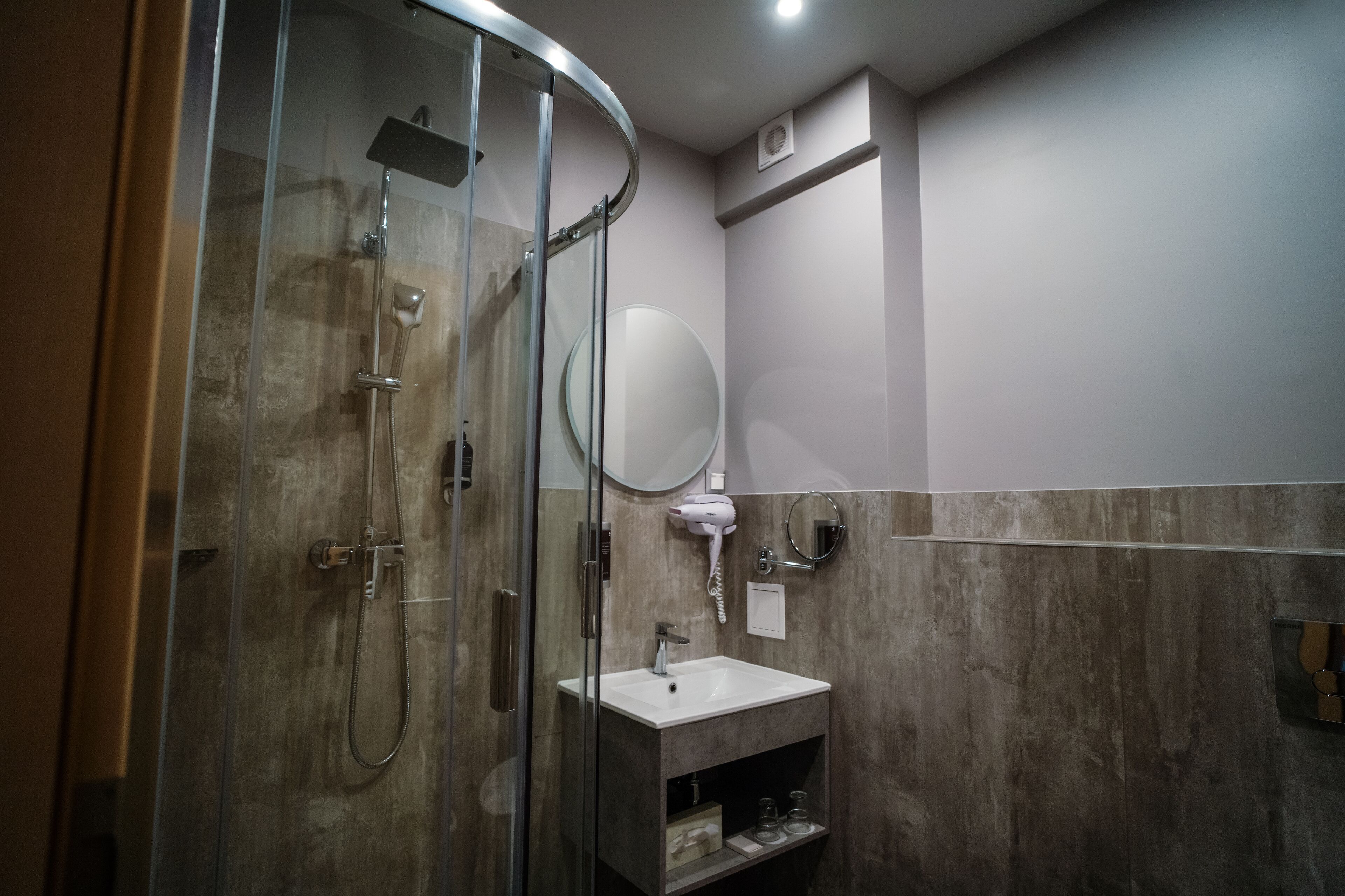A modern bathroom with a glass-enclosed shower, a white sink, and a round mirror.
