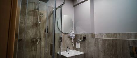 A modern bathroom with a glass-enclosed shower, a white sink, and a round mirror.