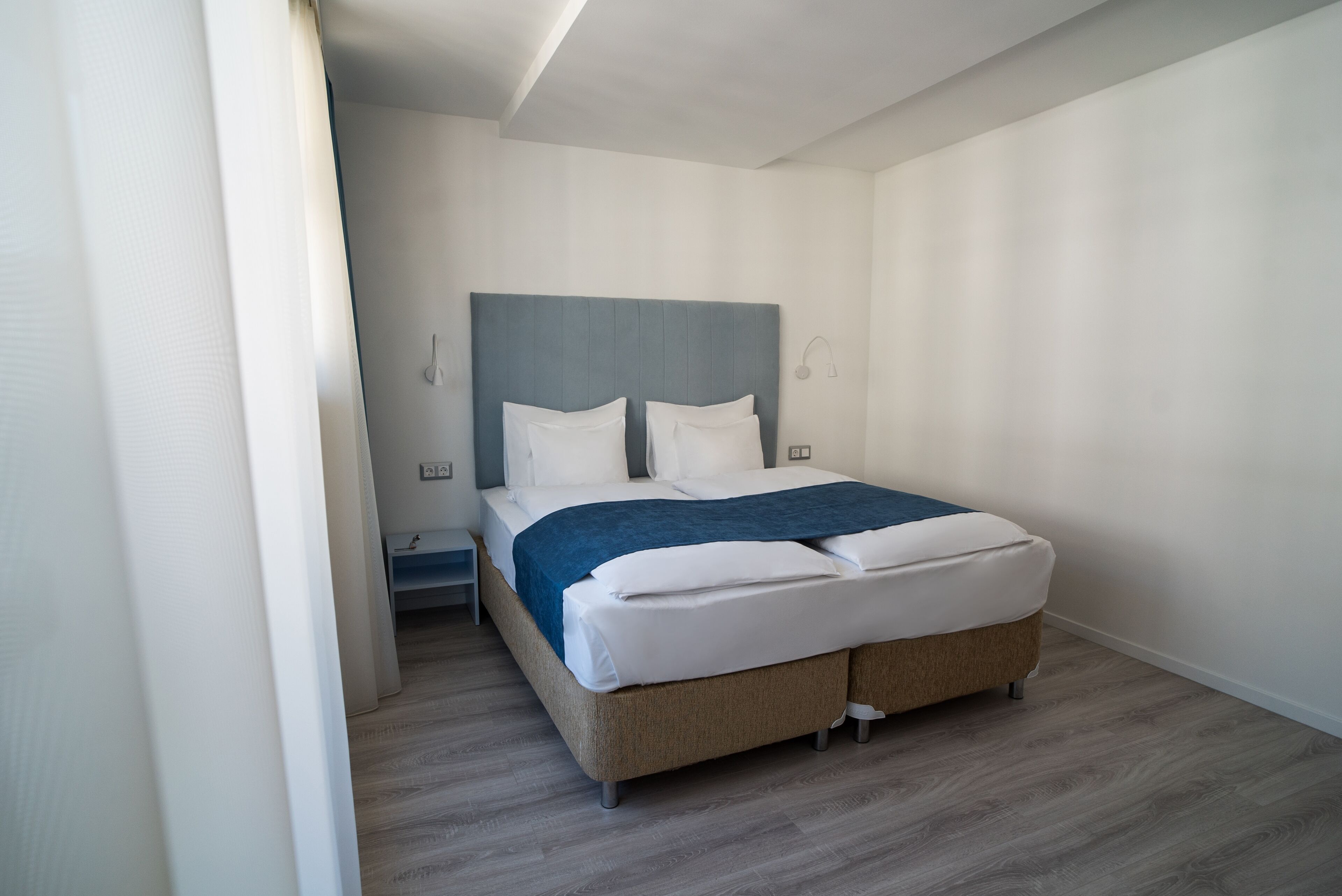 A modern bedroom with a bed, a nightstand, and a wall-mounted lamp.