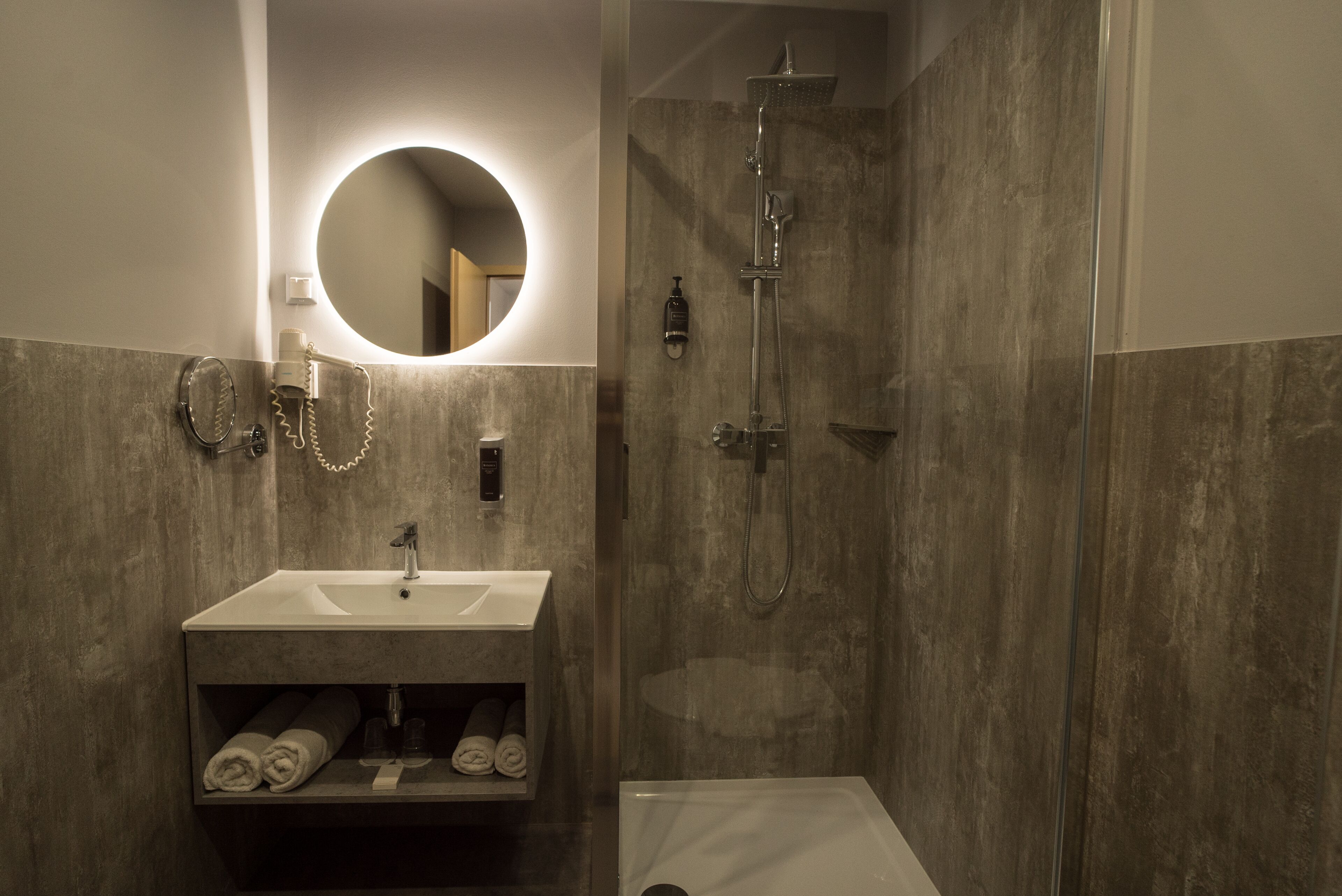 Un baño moderno con lavamanos integrado, un espejo redondo, un cabezal de ducha manual y un inodoro.