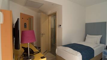 A hotel room with a bed, a desk with a lamp, a telephone, and a television.