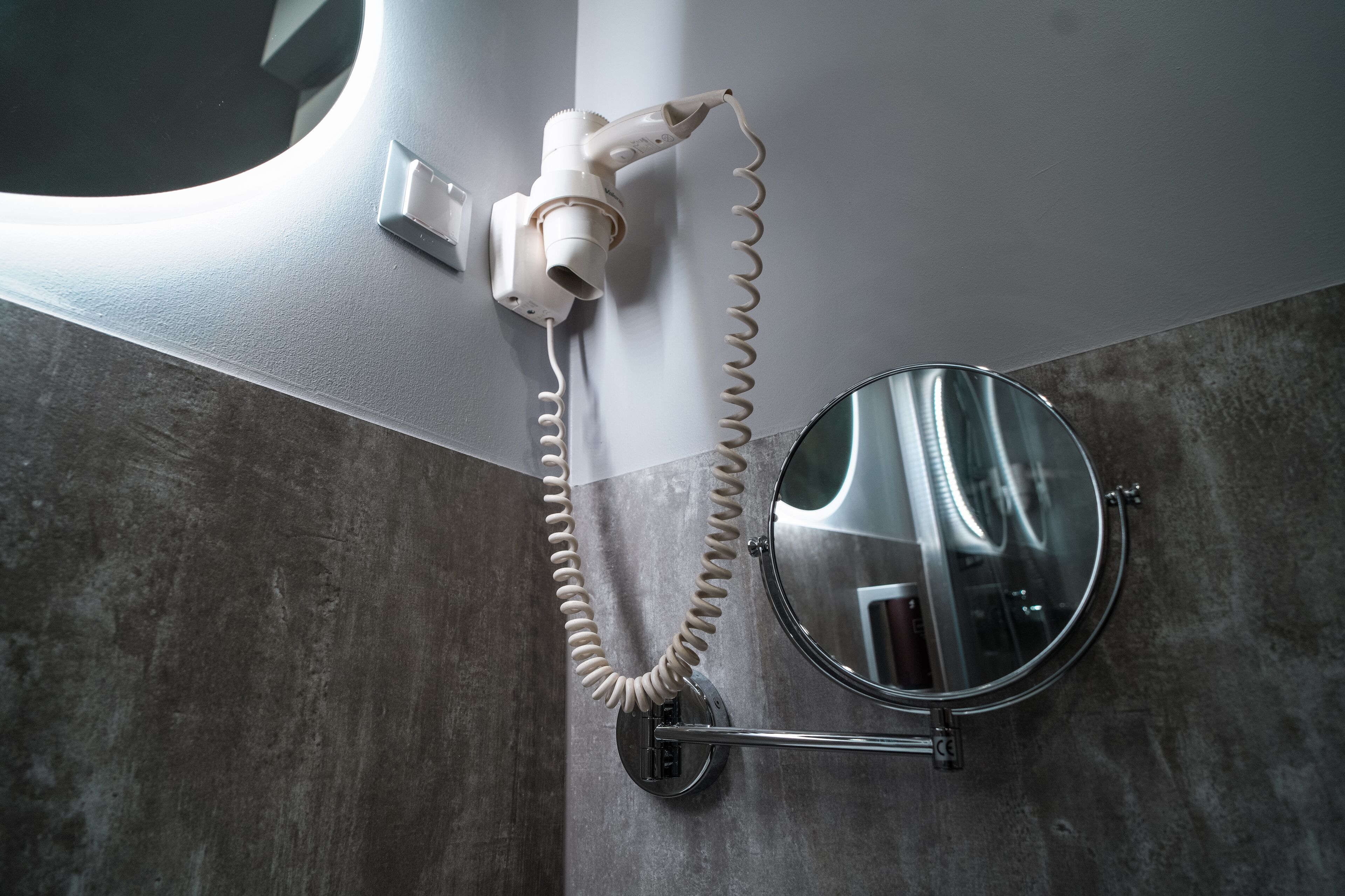 Un baño con un secador de pelo fijado en la pared, un espejo redondo y un perchero para toallas.