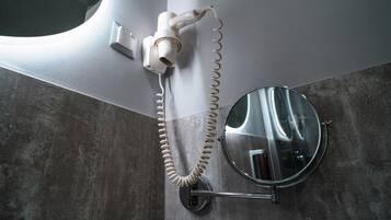 Un baño con un secador de pelo fijado en la pared, un espejo redondo y un perchero para toallas.