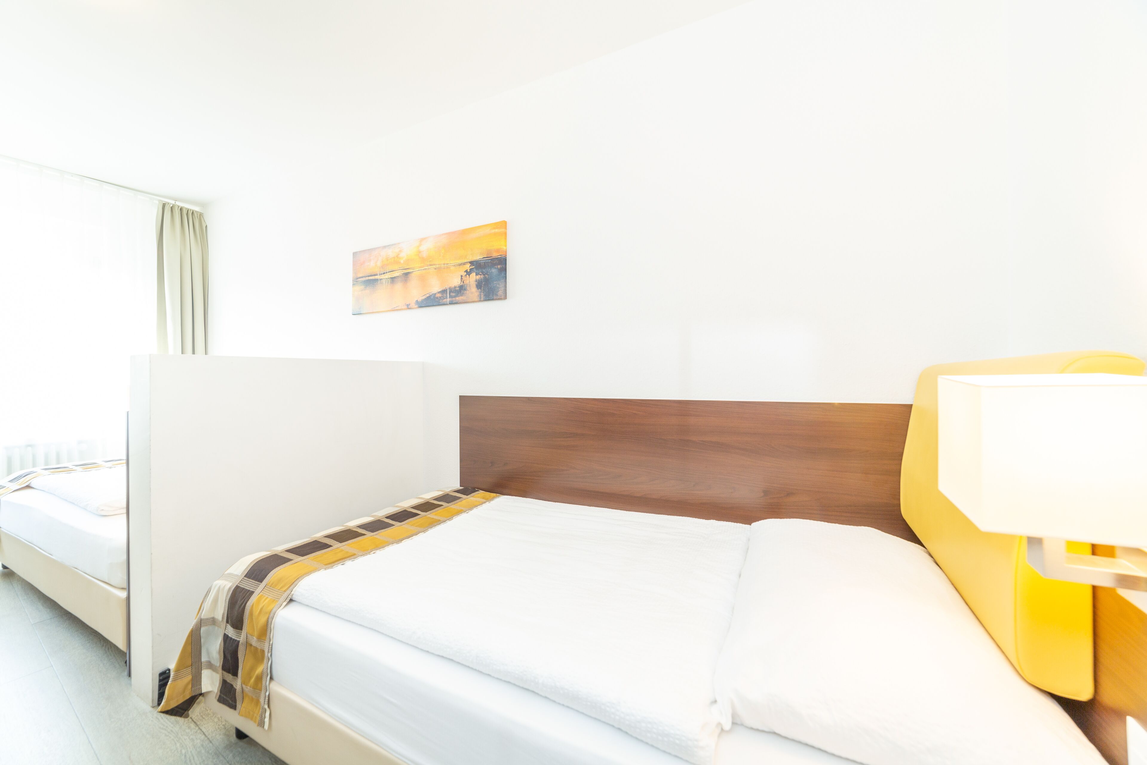 A hotel room with a bed, a bedside lamp, and a painting on the wall.