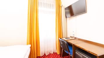 Una habitación de hotel con cama, escritorio, silla, televisor y ventana con cortinas.