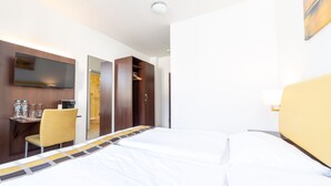 A hotel room with a bed, a desk with a chair, a TV, and a wardrobe. - Hotel Rheinfelderhof (Basel)