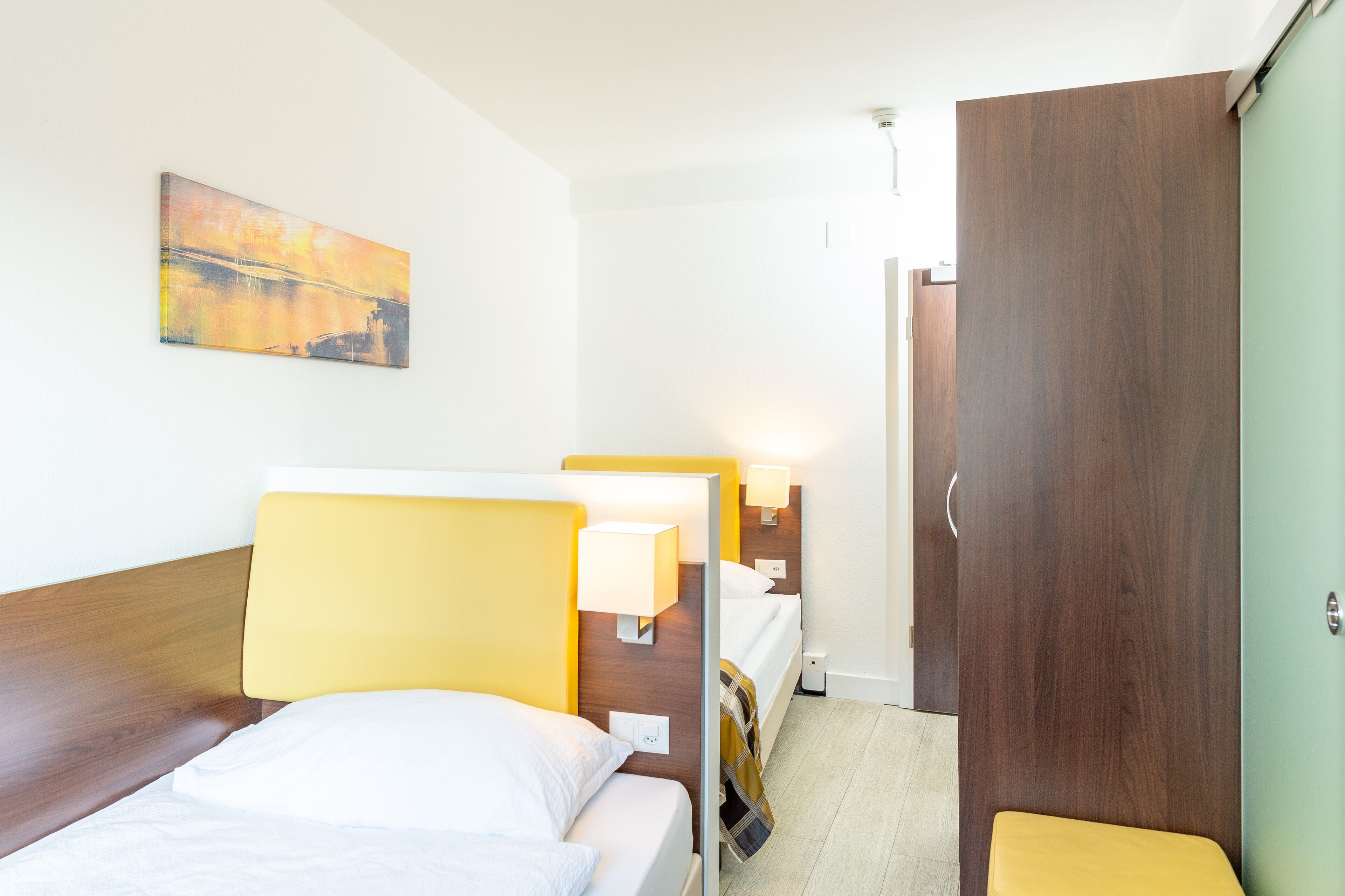 Una habitación de hotel con dos camas, un armario de madera, un cuadro en la pared y lámparas de noche.