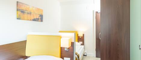 Una habitación de hotel con dos camas, un armario de madera, un cuadro en la pared y lámparas de noche.