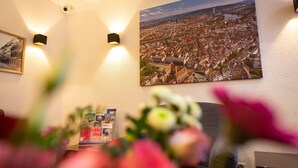 A room with a cityscape poster, two wall-mounted lights, and a floral arrangement. - Hotel Rheinfelderhof (Basel)
