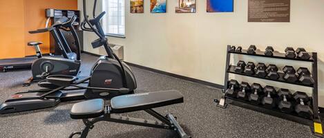 A gym with cardio machines, dumbbells, and a bench.