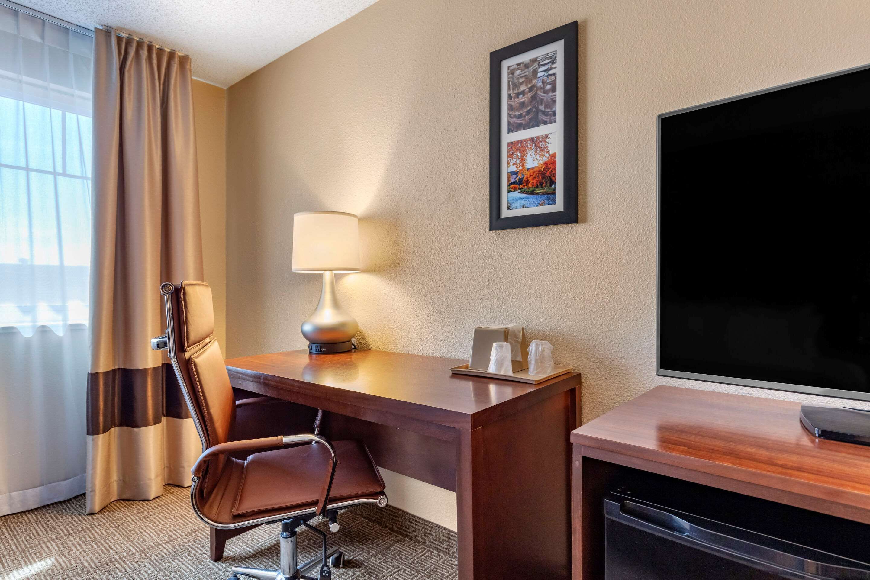 A hotel room with a wooden desk, a chair, a television, a lamp, and a framed picture on the wall.