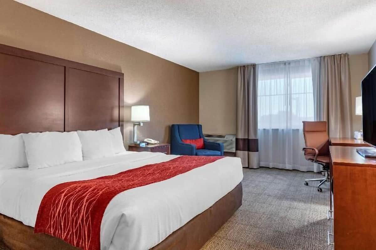 Quarto de hotel com uma cama grande, escrivaninha, cadeira e televisão.