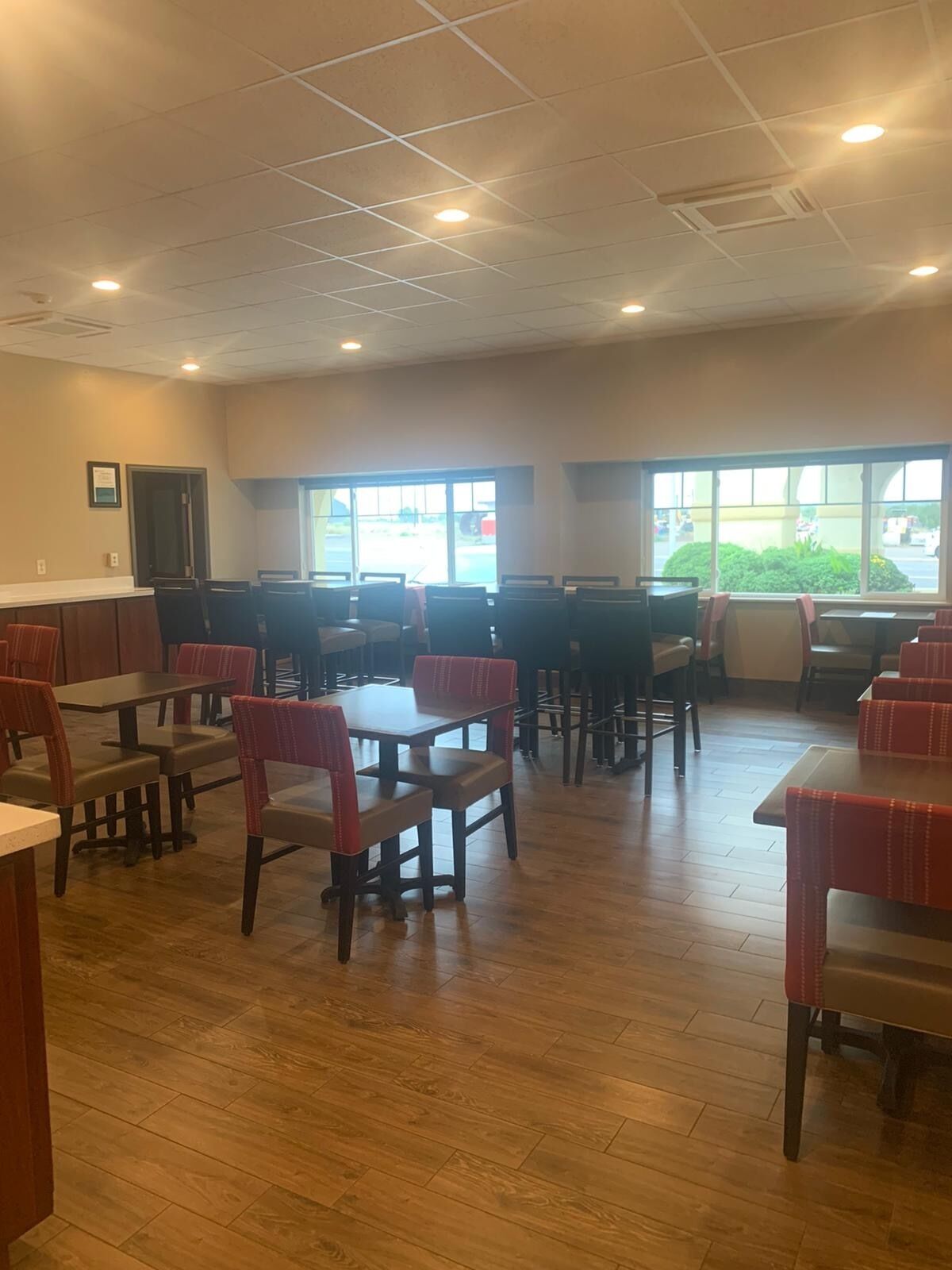 A restaurant interior with booths and tables, wooden flooring, and large windows with a view of the parking lot.