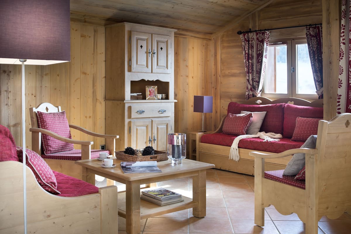 L’intérieur d’un chalet en bois chaleureux et accueillant, avec un canapé, des fauteuils, une table et un buffet.