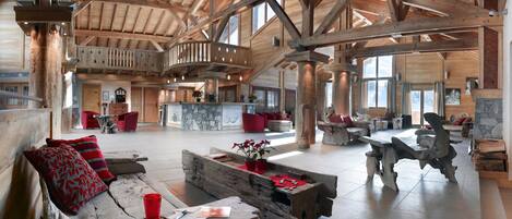 A spacious interior with wooden beams, a stone fireplace, and a high ceiling.