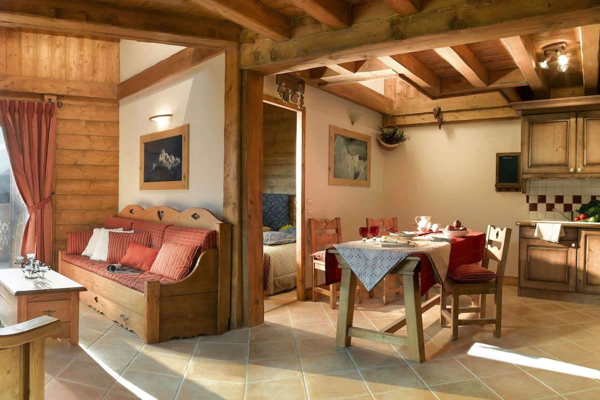 L’intérieur d’un chalet en bois chaleureux et accueillant, avec un coin repas, un canapé doté de coussins rouges et une table mise pour le repas.