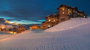 Una cabaña de varios pisos con balcones, ubicada en una ladera cubierta de nieve.