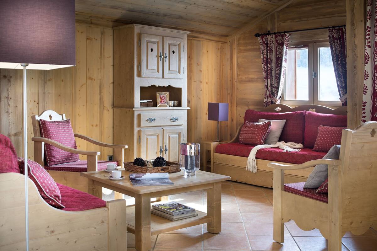 Interior acogedor de una cabaña de madera con sofá, sillas, una mesa y un armario.
