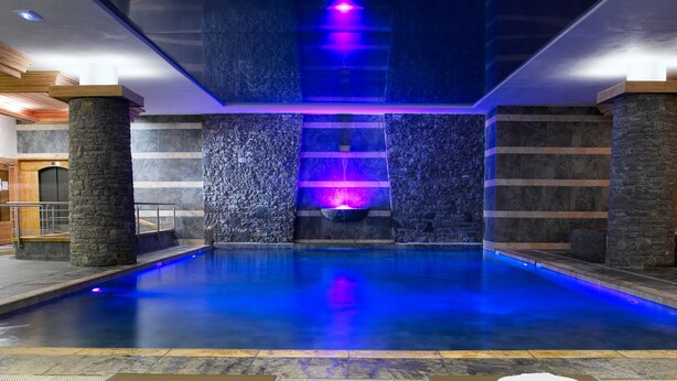 A spa pool area with a stone wall, a water feature, and lounge chairs. - CGH Résidences & Spas Les Granges du Soleil (La Plagne-Tarentaise)