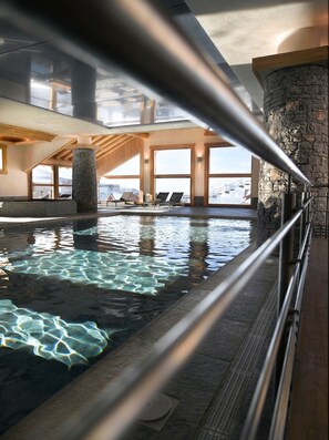 An indoor swimming pool with clear water, stone pillars, and wooden beams. - CGH Résidences & Spas Les Granges du Soleil (La Plagne-Tarentaise)