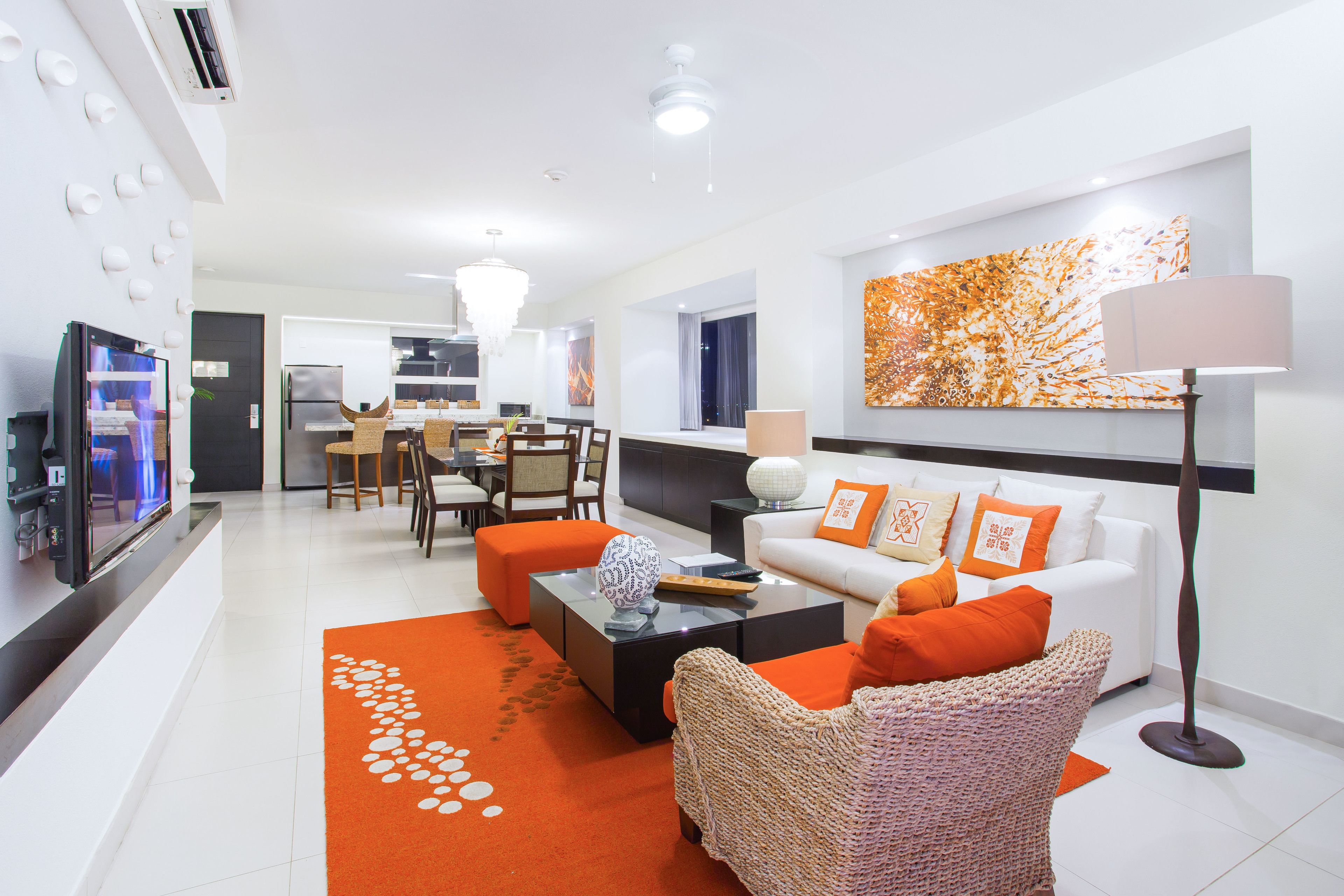 A modern living room with a white sofa, orange cushions, a woven armchair, and a coffee table.