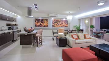 Una sala moderna con sofá, un reposapiés rojo, una zona de comedor con mesa y sillas, y una cocina con microondas y un cesto de aperitivos.