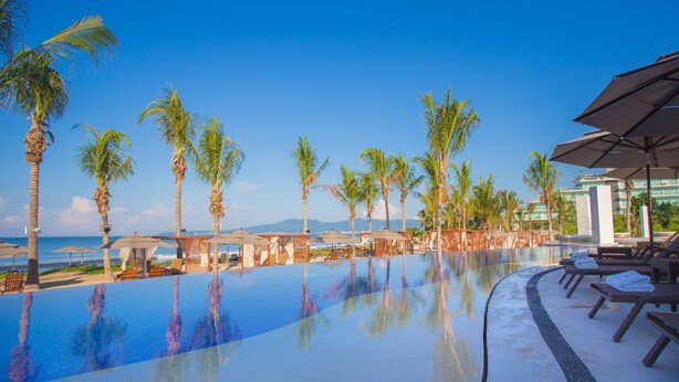 A poolside area with lounge chairs and umbrellas, palm trees, and a view of the ocean. - Marival Distinct All-Inclusive Handwritten Collection (Nuevo Nayarit)