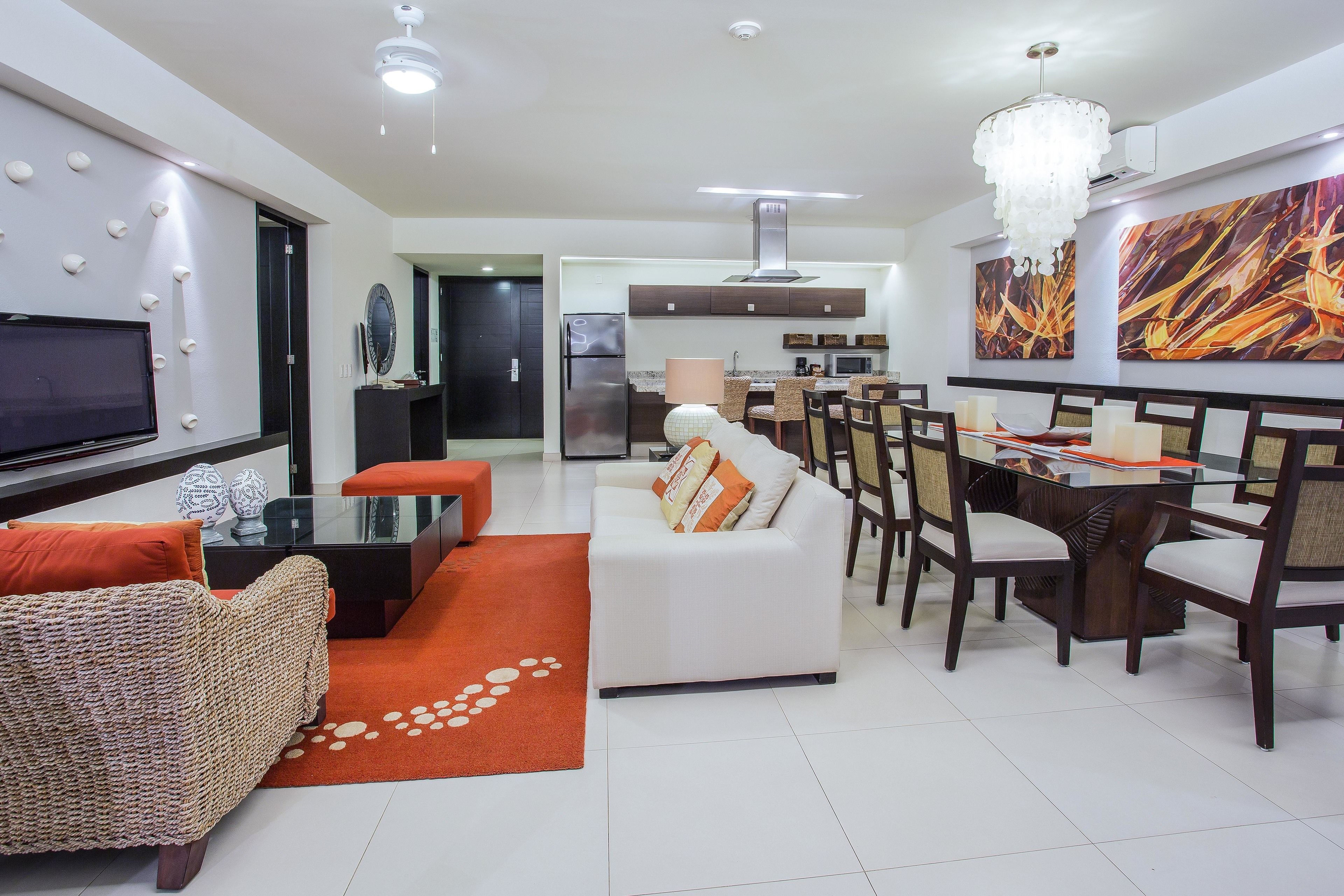 Una sala de estar moderna con un sofá blanco, alfombra naranja y un comedor con sillas de madera y una mesa de vidrio.