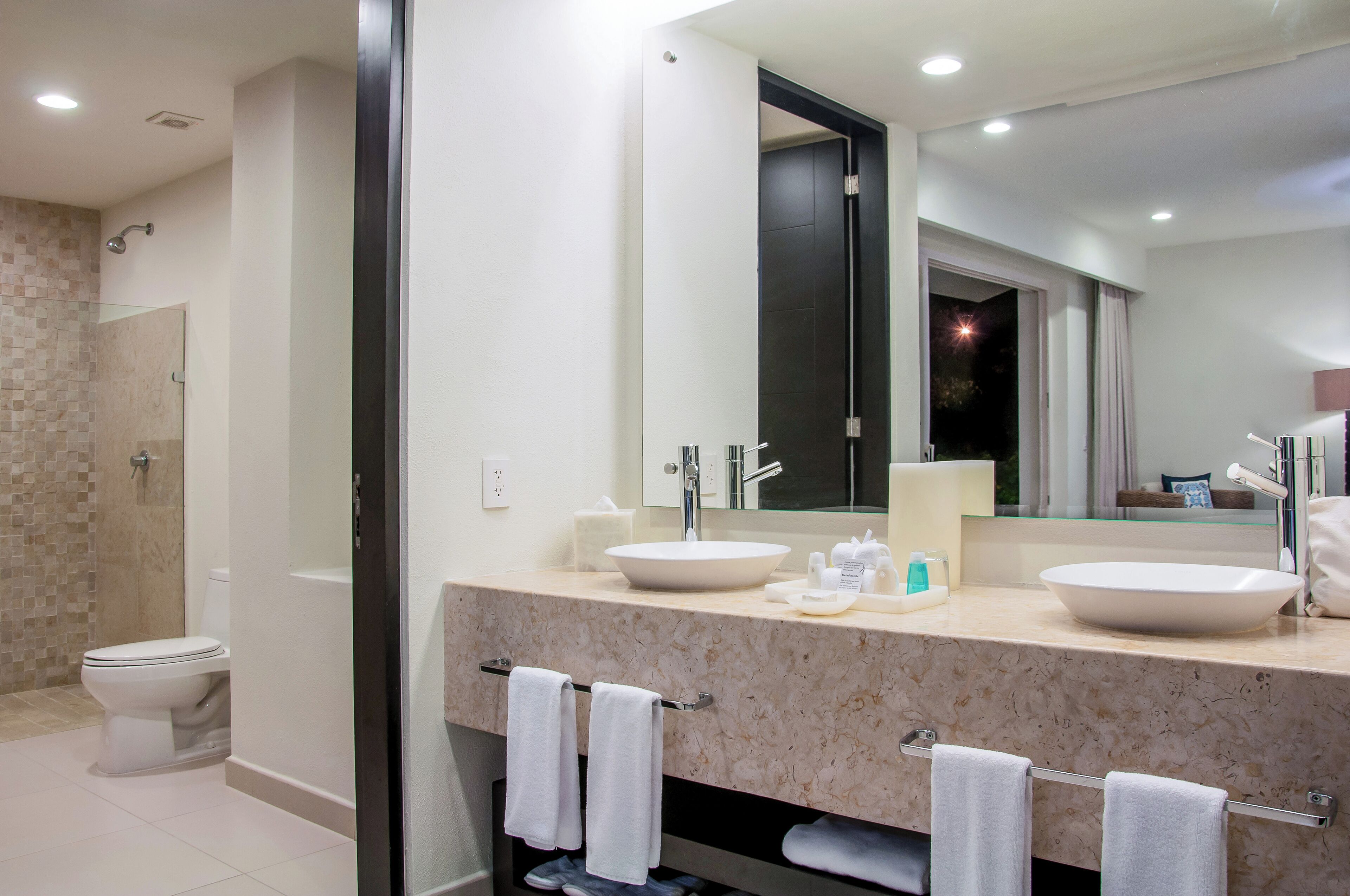 A modern bathroom with two sinks, a large mirror, and a shower area.