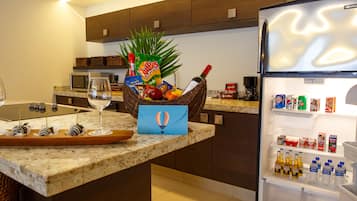A kitchen with a marble countertop, a wicker basket with snacks, a wine glass, and a refrigerator stocked with beverages.