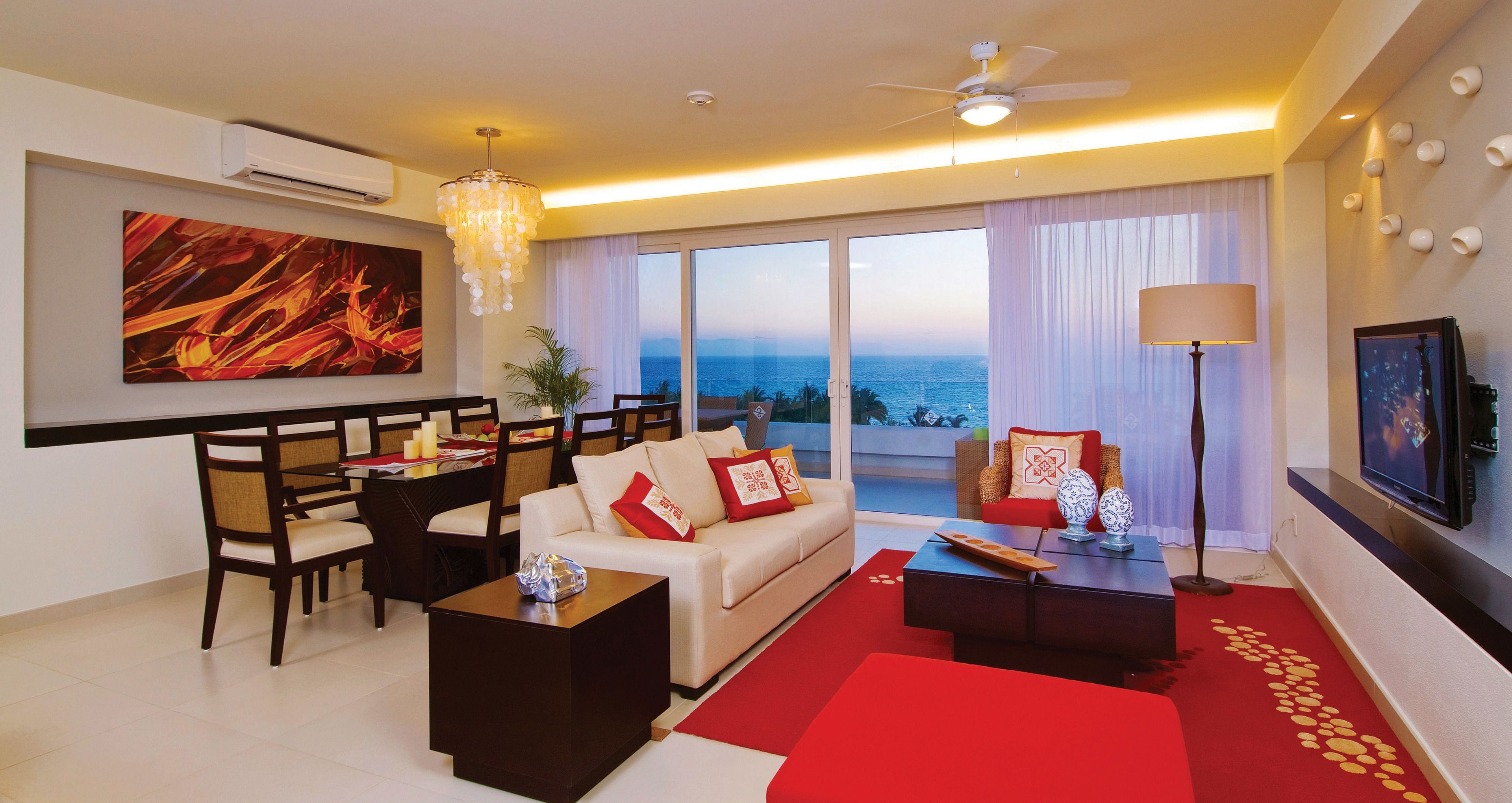 A modern living room with a sofa, coffee table, and dining area. There is a large window with a view of the ocean.