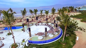 A resort with a circular pool surrounded by lounge chairs and umbrellas, a beach area with palm trees, and a view of the ocean. - Marival Distinct All-Inclusive Handwritten Collection (Nuevo Nayarit)