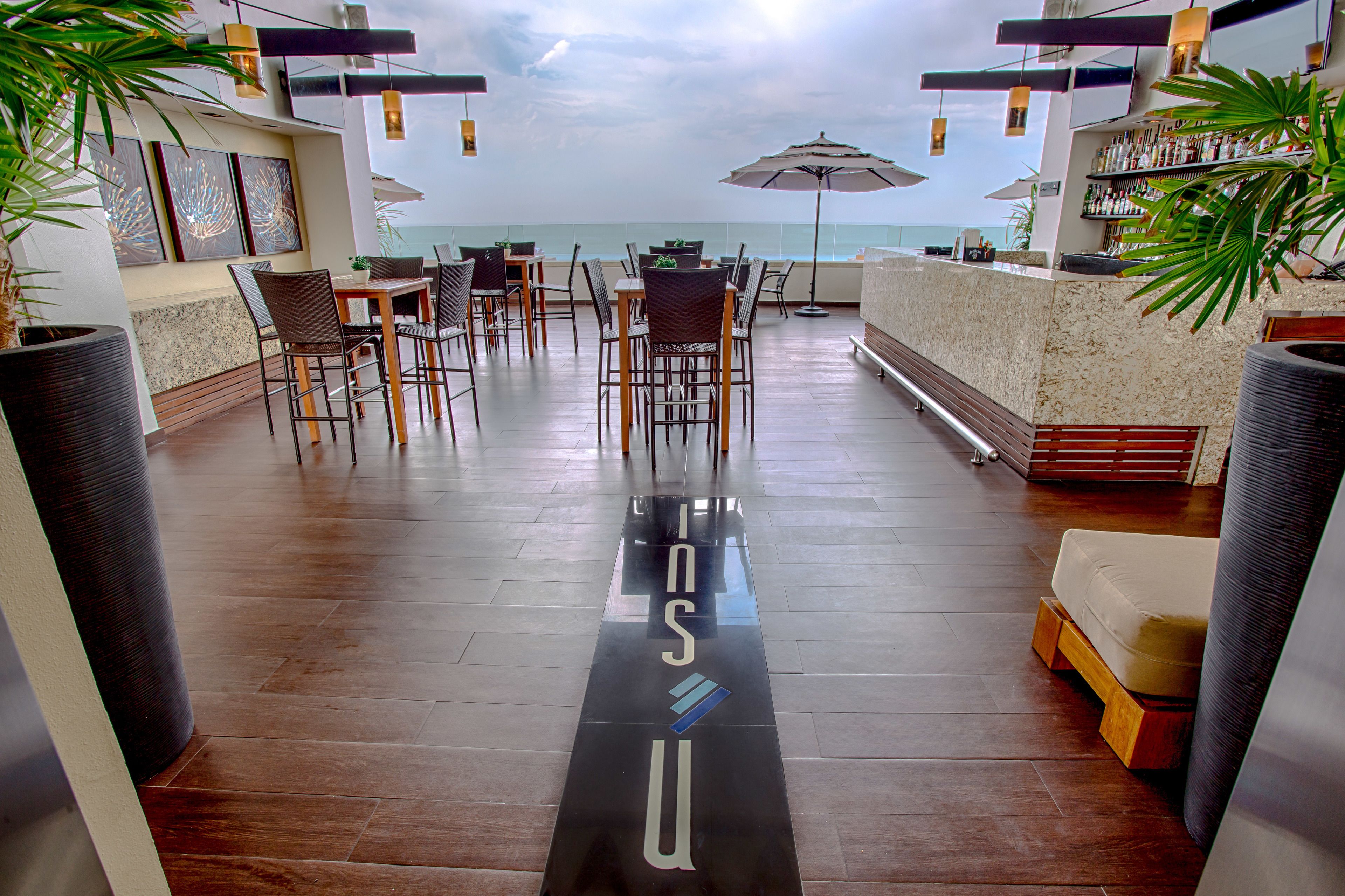 A spacious outdoor seating area with a view of the ocean, featuring tables and chairs, umbrellas, and a bar area.