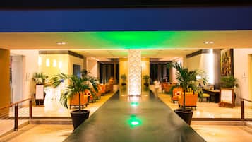 Un vestíbulo de hotel con piso reflectante en el centro, zonas de estar y plantas en macetas.