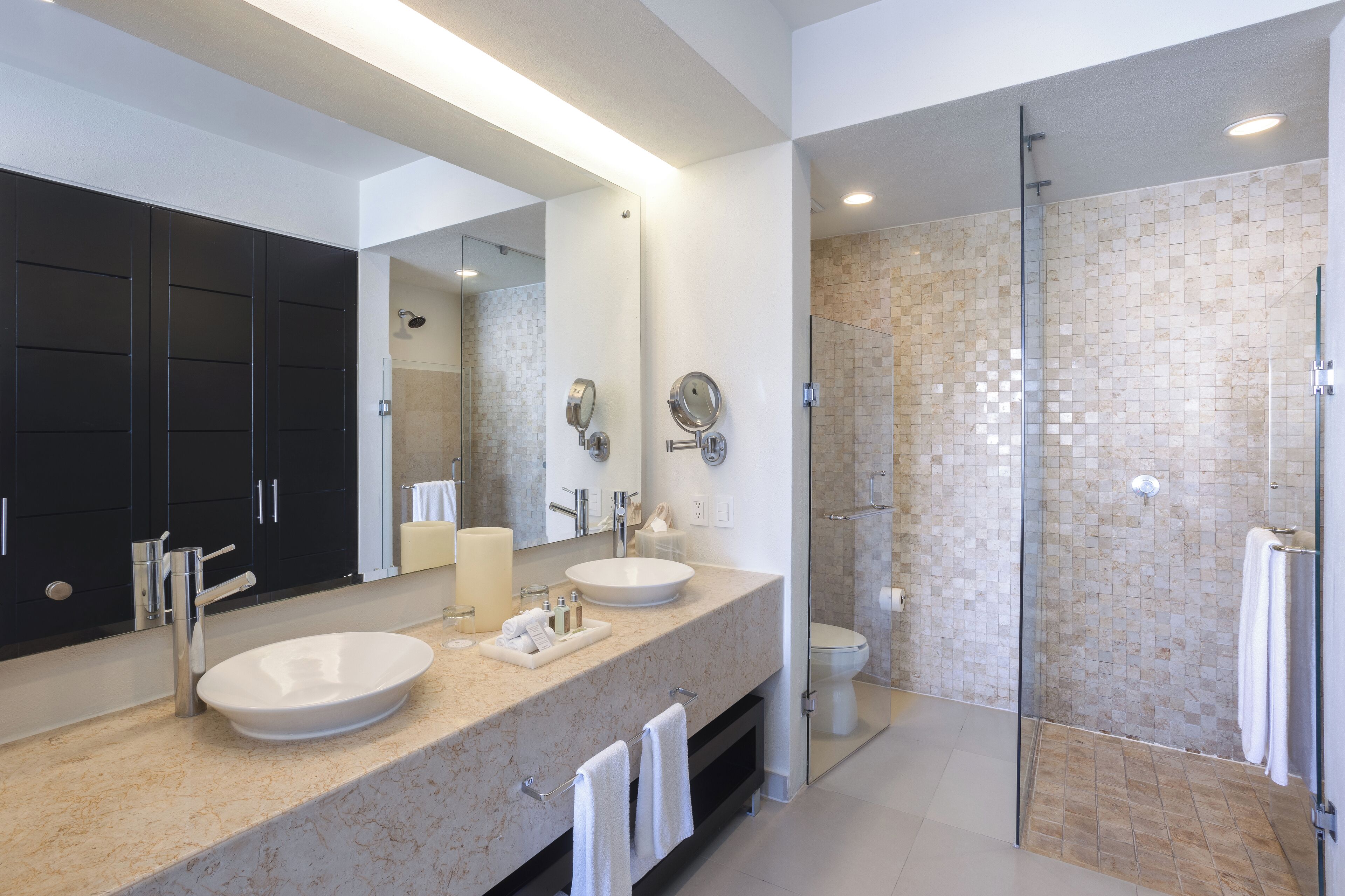 Un baño moderno con dos lavamanos, un espejo grande y una ducha con paredes de vidrio.