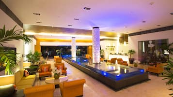 A modern lobby with a central pool, comfortable seating, and a reception area.
