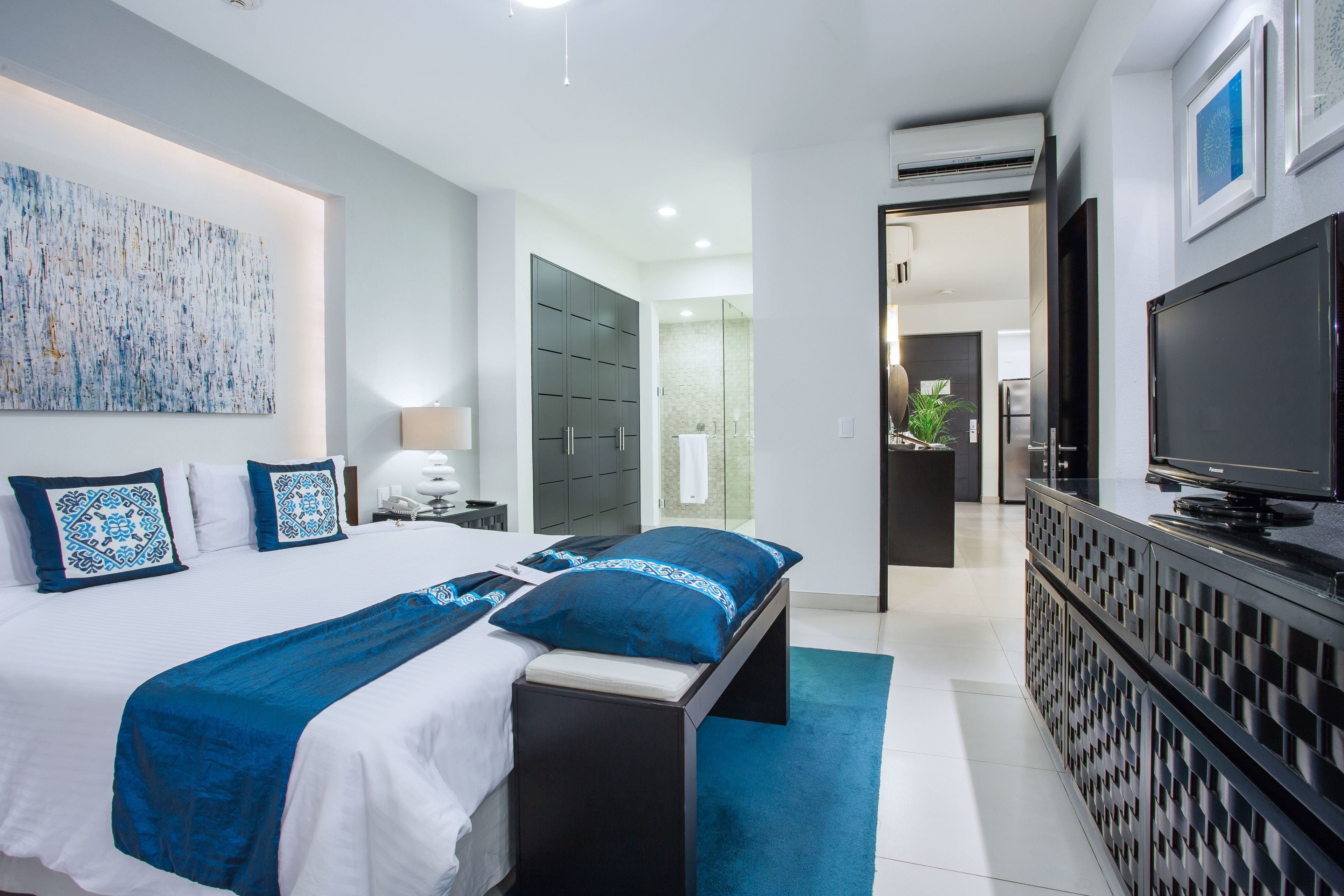 A modern hotel room with a large bed, a TV, and a bathroom visible through an open door.