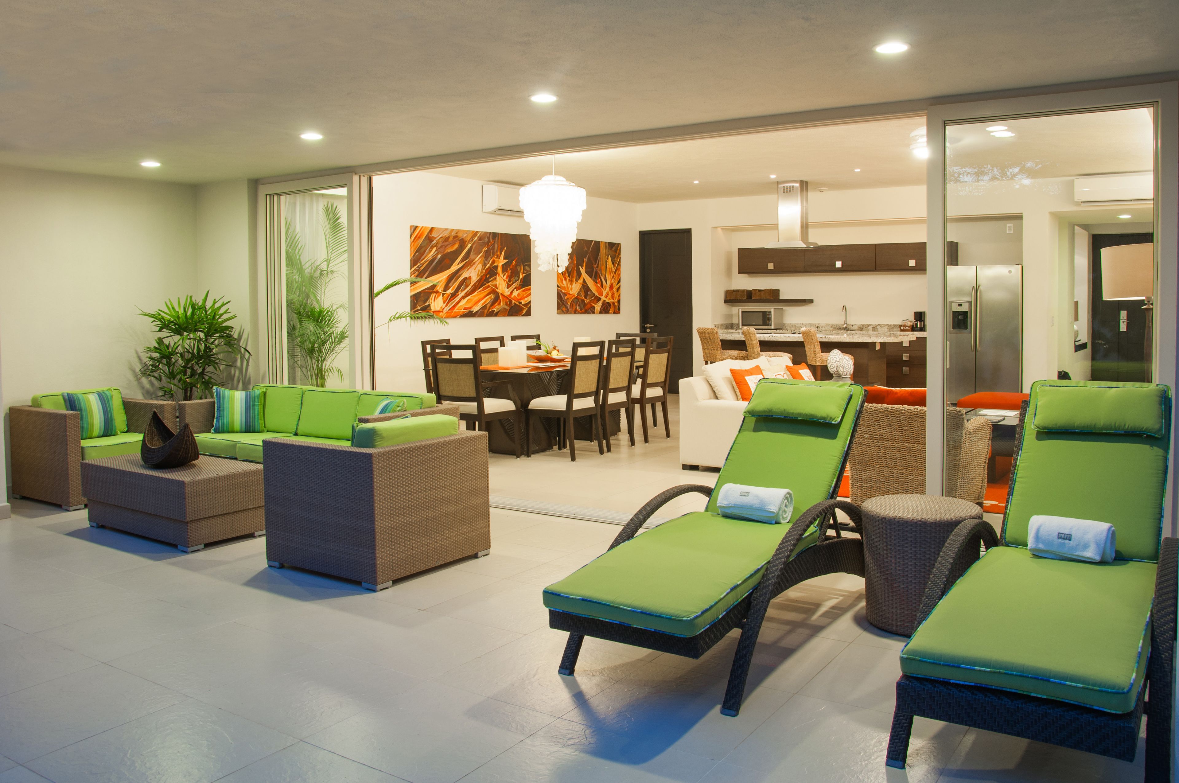 Una sala de estar moderna con sofás acolchados verdes, un comedor y una cocina al fondo.