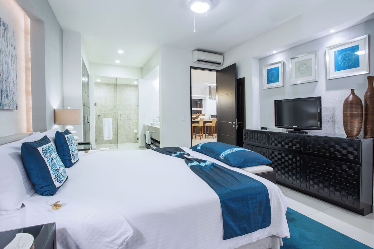 Ein modernes Hotelzimmer mit einem großen Bett, einem Fernseher, einer Minibar und einem durchgegangenen Tür erkennbaren Badezimmer.