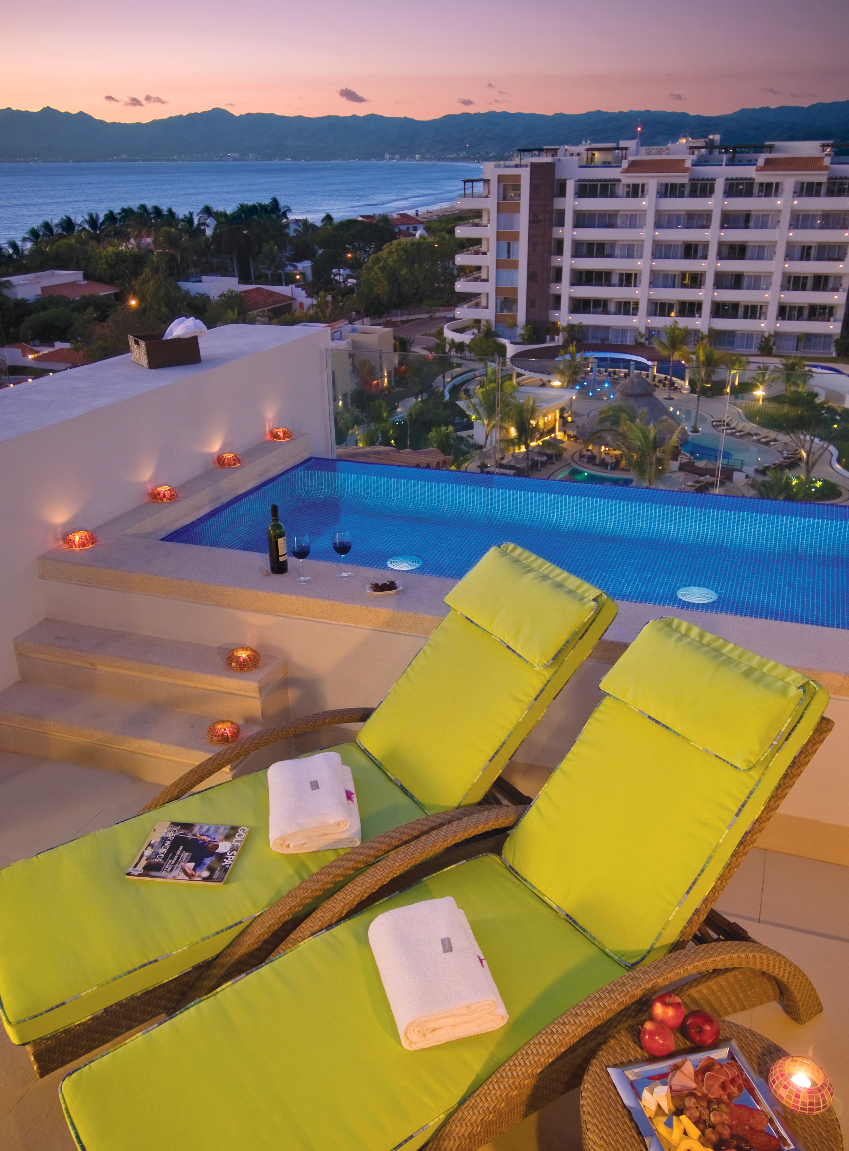 Un espace piscine aménagé sur le toit, avec des chaises longues, une piscine et une vue sur l’océan et les montagnes.
